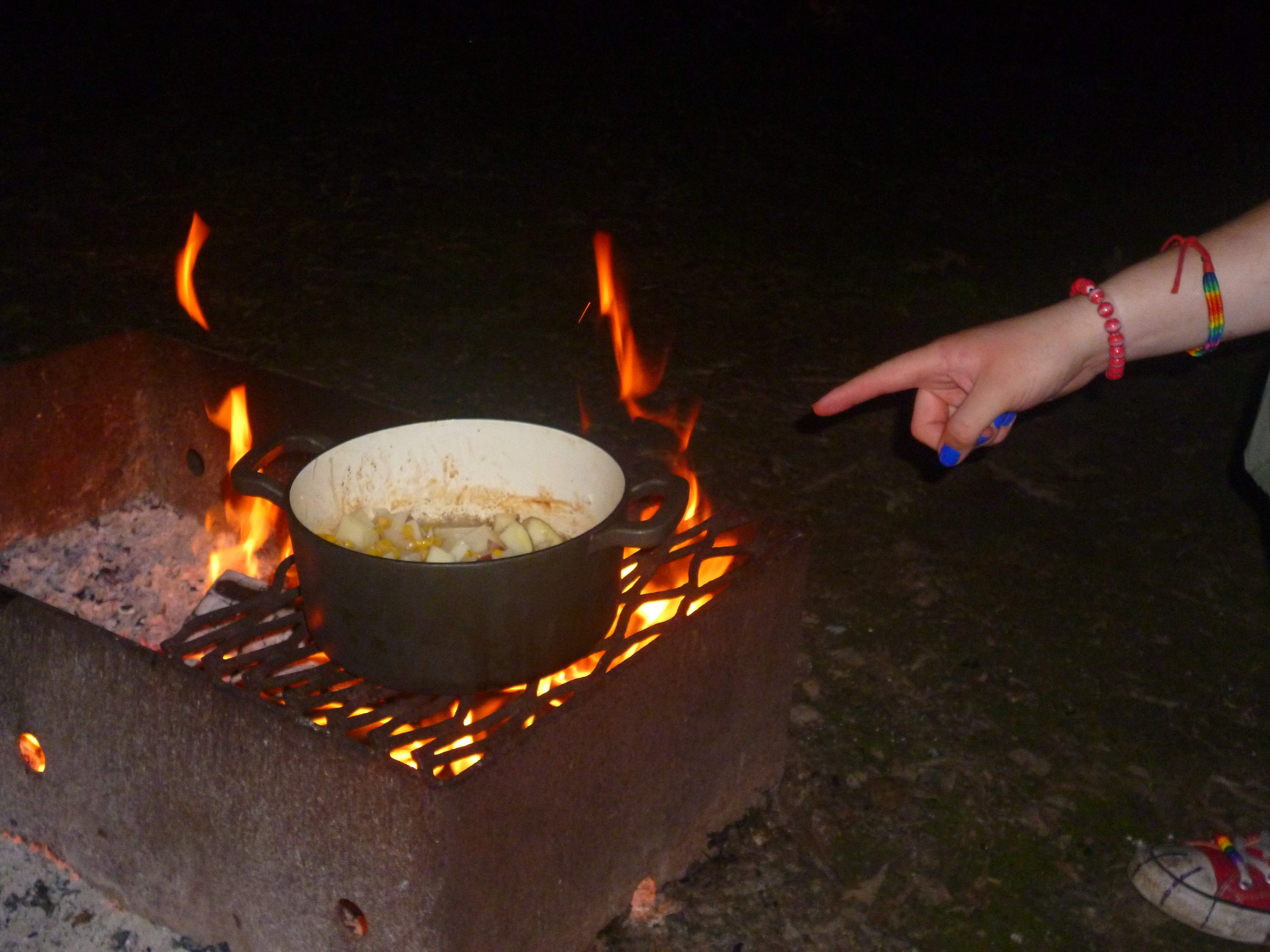 A pot of soup on the grill above a fire pit.